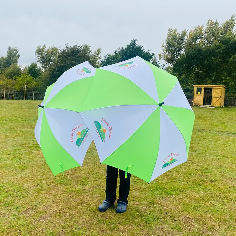 Full size promotional golf umbrella for printing. Green & white panels. Full colour print. No minimum order. Photo of green umbrellas in garden.